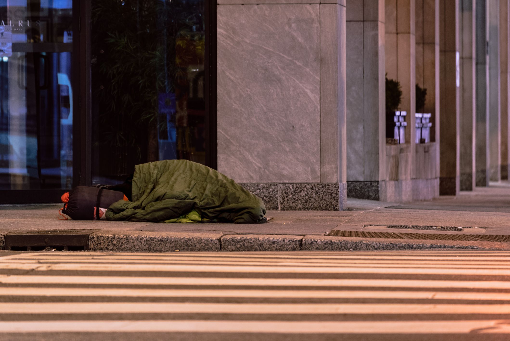 An unhoused person sleeps on the sidewalk in a sleeping bag on a cold winter night in Toronto.