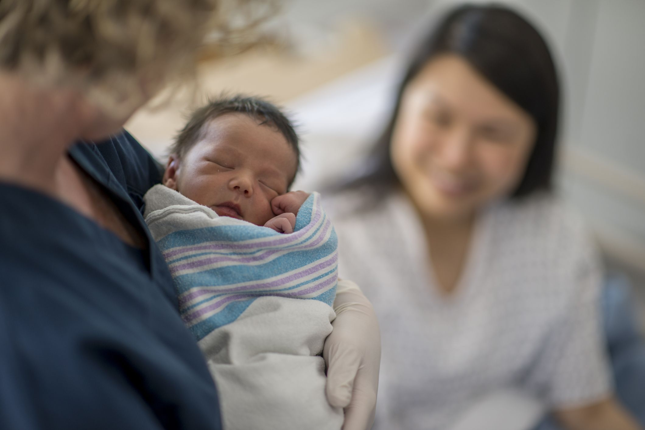 A newborn baby is held while a woman watches on.